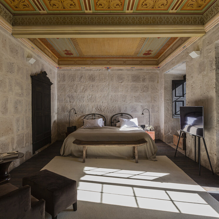 Hotelzimmer mit historisch bemalter Holzdecke, Sillar-Steinwaenden und Doppelbett im CIRQA Arequipa.