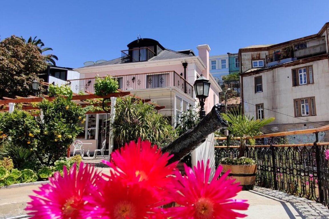 Blick ueber pinke Blumen auf die Hotelterrasse und das historische Gebaeude in Valparaiso.