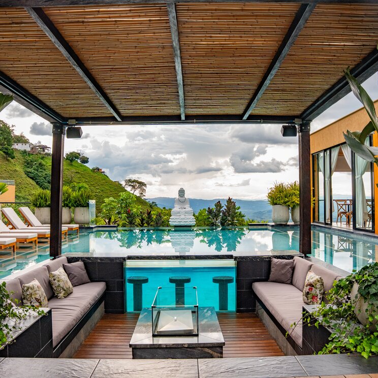 Infinity-Pool mit Buddha-Statue, Sitzlounge und weitem Talblick in Lateinamerika.