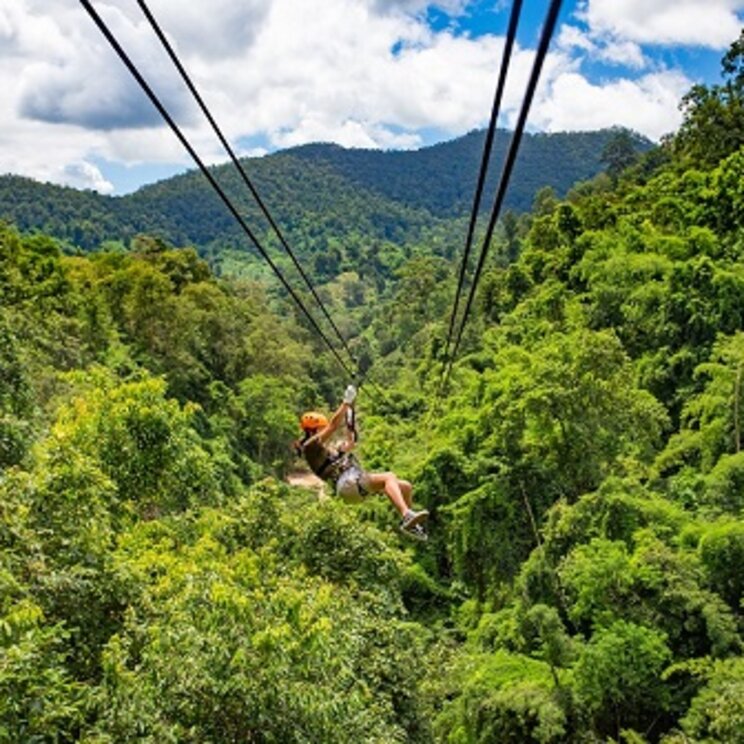 Person beim Ziplining über den dichten Regenwald mit Blick auf grüne Hügel in Belize