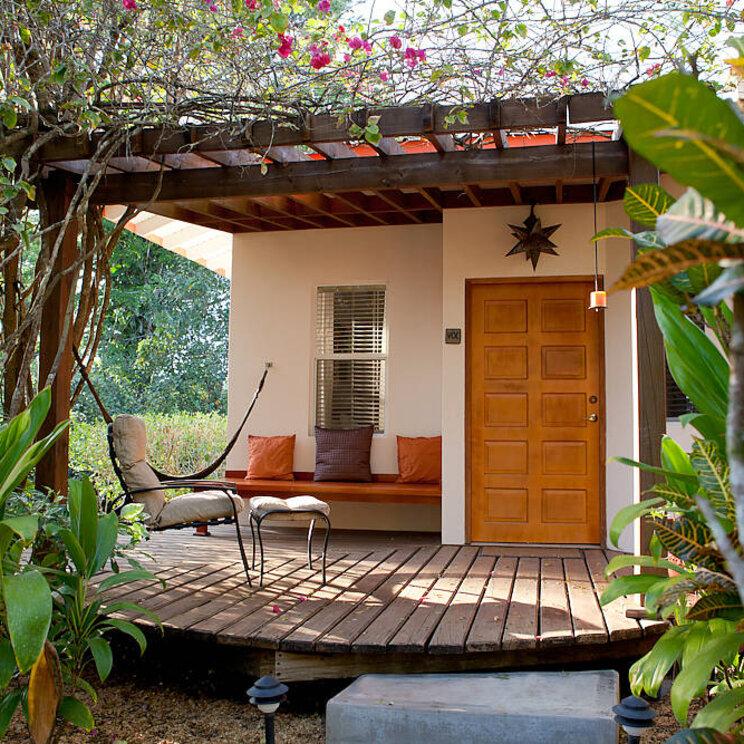 Bungalow im Ka'ana Resort in San Ignacio, Belize mit Holzterrasse, Sitzbank und umgeben von tropischer Vegetation.
