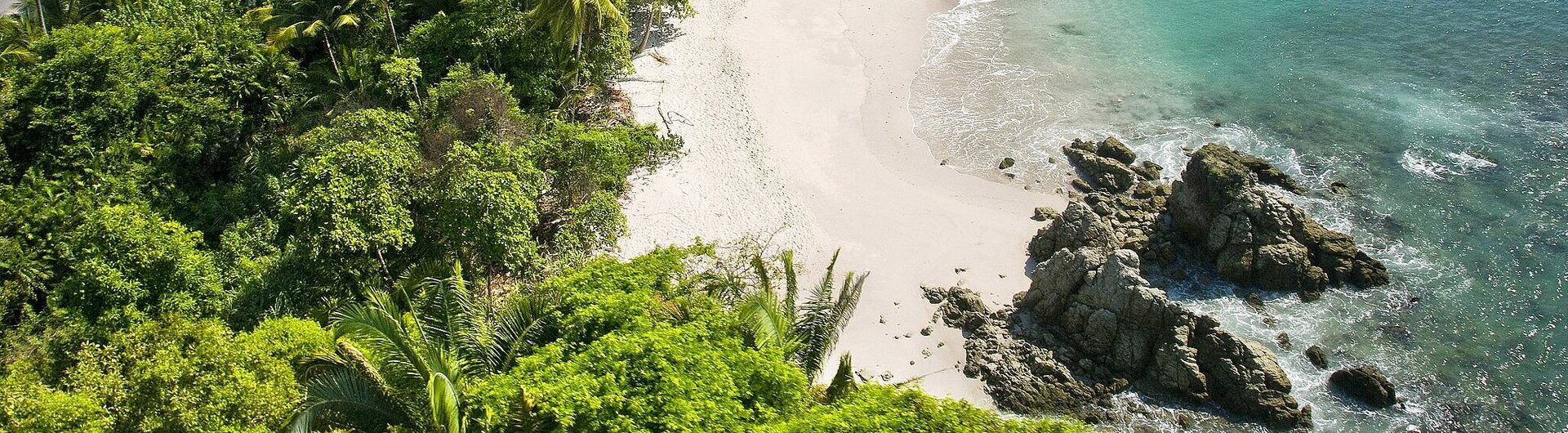 Blick von oben auf eine idyllische Bucht mit türkisfarbenem Wasser, weißem Sandstrand und üppigem Regenwald, Felsen im Vordergrund, weitere Bucht im Hintergrund in Manuel Antonio, Costa Rica