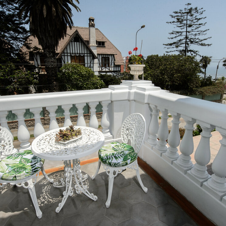 Balkon mit weißen Metallmoebeln, Balustrade und Blick auf ein Nachbarhaus im Hotel Villa Barranco in Lima, Peru.