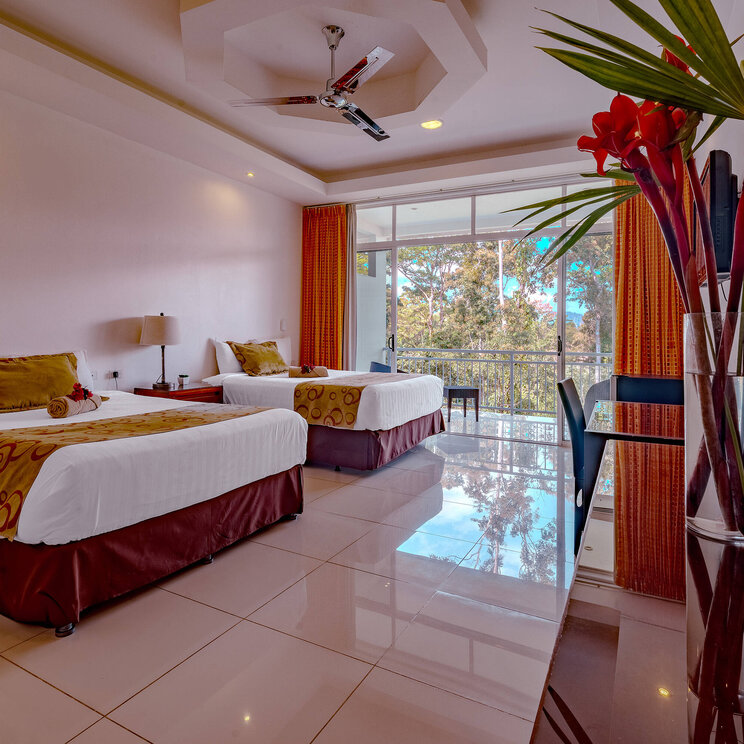 Modernes Zimmer im Hotel Villa Florencia in Costa Rica mit zwei Doppelbetten, großen Fenstern und Blick ins Grüne.
