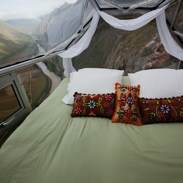 Innenansicht einer transparenten Kapsel am Fels mit Doppelbett und Blick auf das Heilige Tal in Peru.