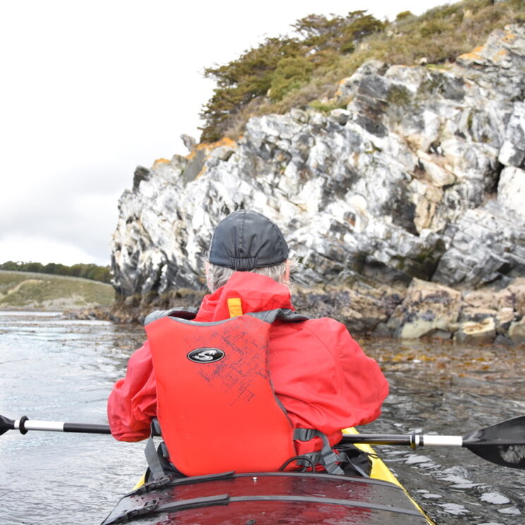 Kajakfahrer mit roter Schwimmweste paddelt entlang der felsigen Küste der Isla Navarino in Patagonien, Chile.