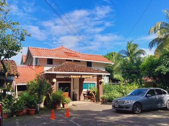 Außenansicht des Hotel Villa Paraíso auf der Insel Ometepe, Nicaragua, mit rotem Ziegeldach, tropischer Bepflanzung und Parkplatz vor dem Eingang.