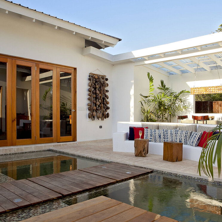 Modern gestalteter Innenhof im Ka'ana Resort in San Ignacio, Belize mit Holzstegen über einem flachen Wasserbecken, Lounge-Bereich und stilvollem Dekor.