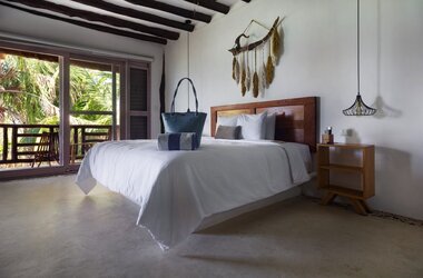 Helles Hotelzimmer mit Holzbalkendecke, Doppelbett und Wanddekoration auf Holbox