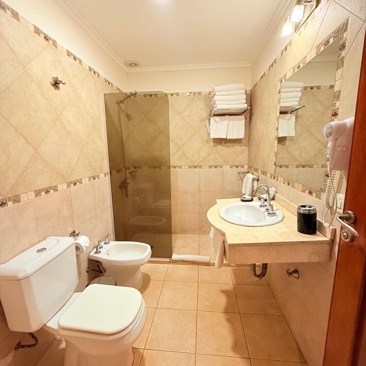 Hell gefliestes Badezimmer mit Waschtisch, Spiegel, Haartrockner, Toilette, Bidet und Dusche in einer Lodge in Iguazo.
