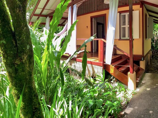 Gelb gestrichener Holzbungalow auf Stelzen umgeben von dichtem tropischem Grün in Puerto Viejo, Costa Rica.