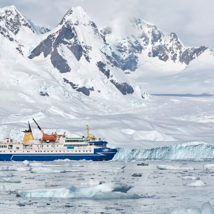 Expeditionsschiff Ocean Nova in der Antarktis zwischen Treibeis und Eisbergen vor schneebedeckten Bergen.