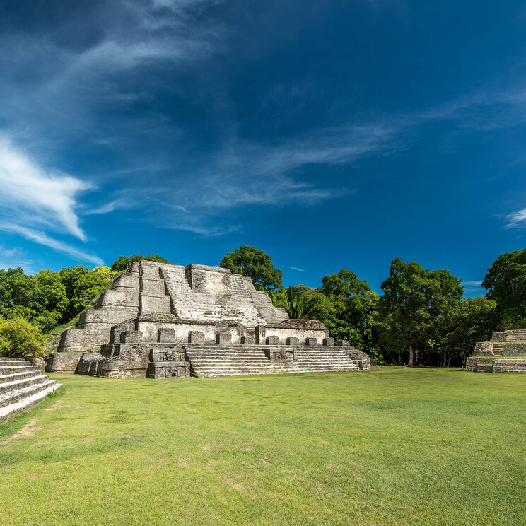 Antike Mayaruinen von Altun Ha in Belize mit imposanten Steintempeln, umgeben von grüner Vegetation und blauem Himmel.
