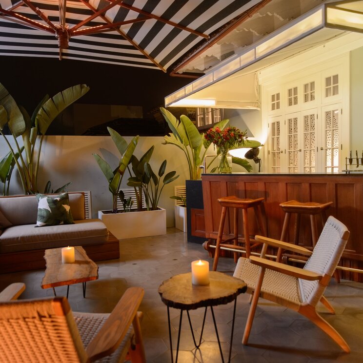 Beleuchtete Terrasse mit Holzbar, Sesseln, Sofa, Kissen, Kerzen und Pflanzen im Hotel Villa Barranco in Lima, Peru.