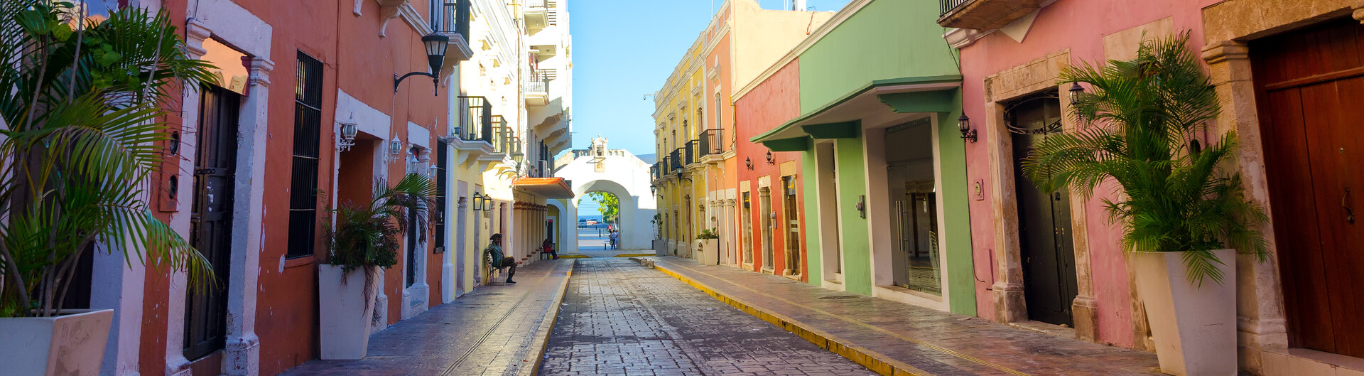 Kolonialstraße im historischen Zentrum von Campeche mit bunten Fassaden, Balkonen und Blick auf ein Stadttor.