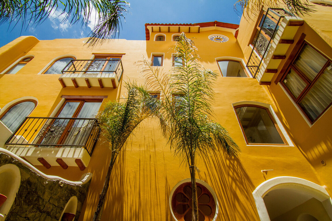 Außenansicht des Hotel Santa Isabella in Riobamba, Ecuador, mit gelber Fassade, dekorativen Balkonen und Palmen vor blauem Himmel.