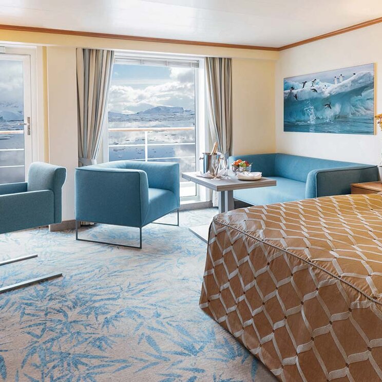 Suite an Bord der Ocean Seaventure Antarktis Expeditionskreuzfahrt mit Wohnbereich, großem Bett, Balkon und Panoramablick auf Eisberge und Meer.