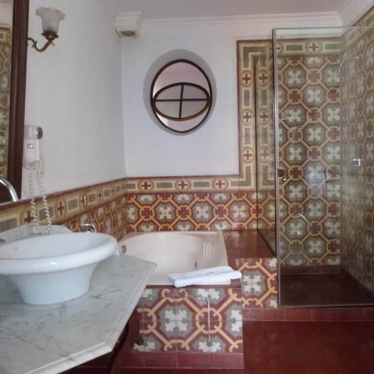 Badezimmer in Sucre mit verzierten Fliesen, Marmorwaschtisch, eingelassener Badewanne und Glasdusche in Bolivien.