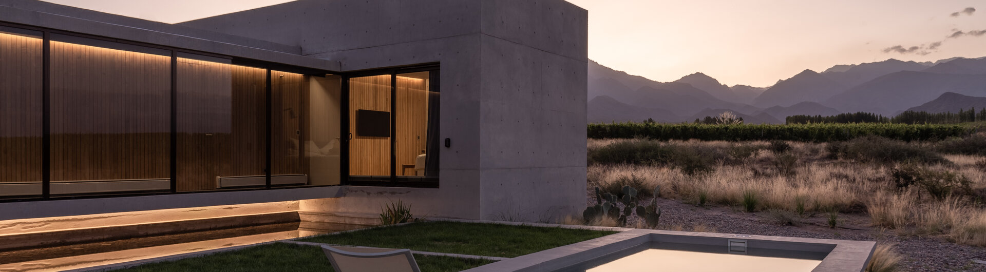 Moderne Betonvilla in Argentinien mit Pool, Sonnenliegen und Bergblick in der Abenddämmerung.