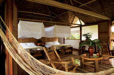 Geraeumige Suite mit Holzwaenden, Reetdach, Betten mit Moskitonetzen und Haengematte in Peru.