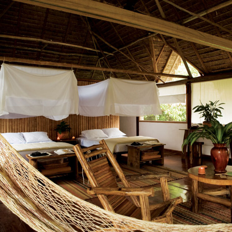 Geraeumige Suite mit Holzwaenden, Reetdach, Betten mit Moskitonetzen und Haengematte in Peru.