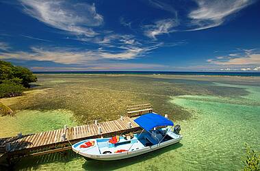 South Water Caye in Belize: Boot am Bootssteg aus Holz mit blauer Himmel und türkisfarbenem Meer im Hintergrund