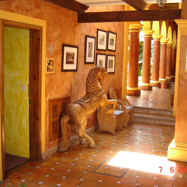 Flur mit Fliesenboden, Wandbildern und großer Holzpferd-Skulptur im Hotel Casa Mexicana in San Cristobal, Mexiko.