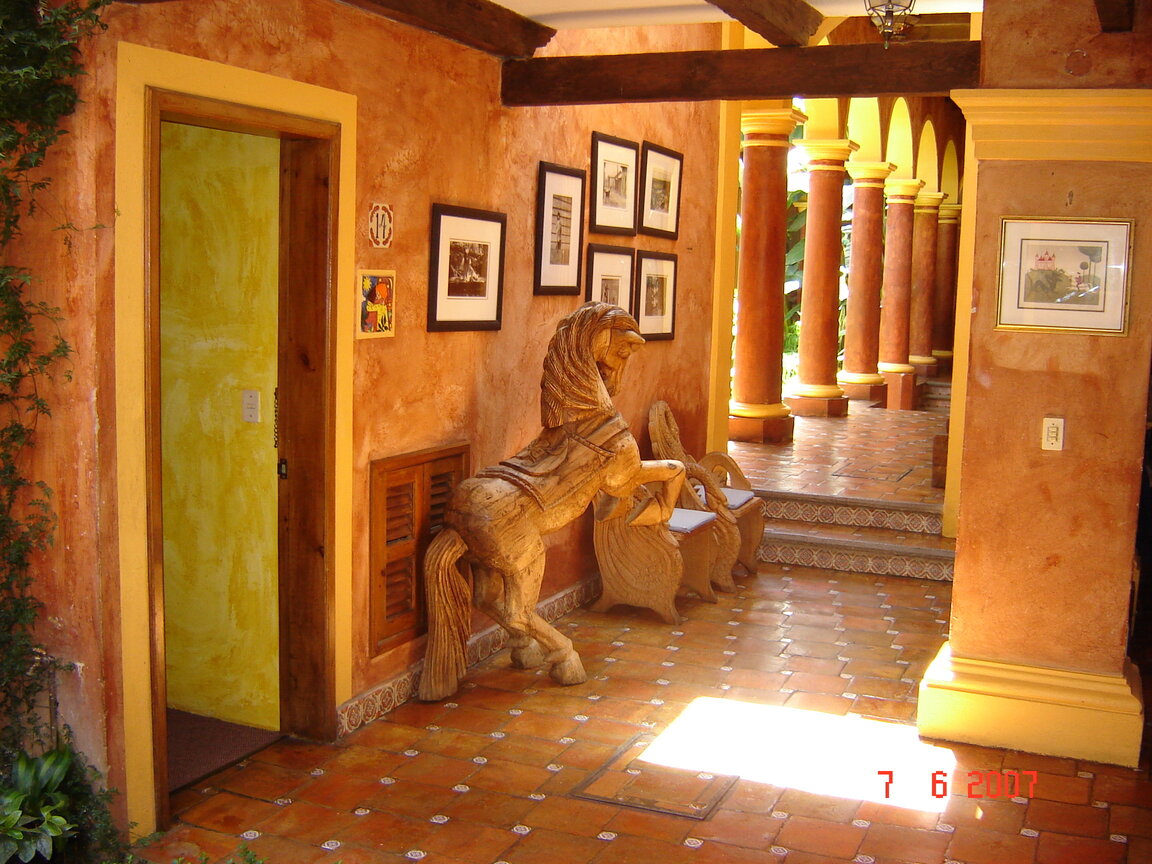 Flur mit Fliesenboden, Wandbildern und großer Holzpferd-Skulptur im Hotel Casa Mexicana in San Cristobal, Mexiko.