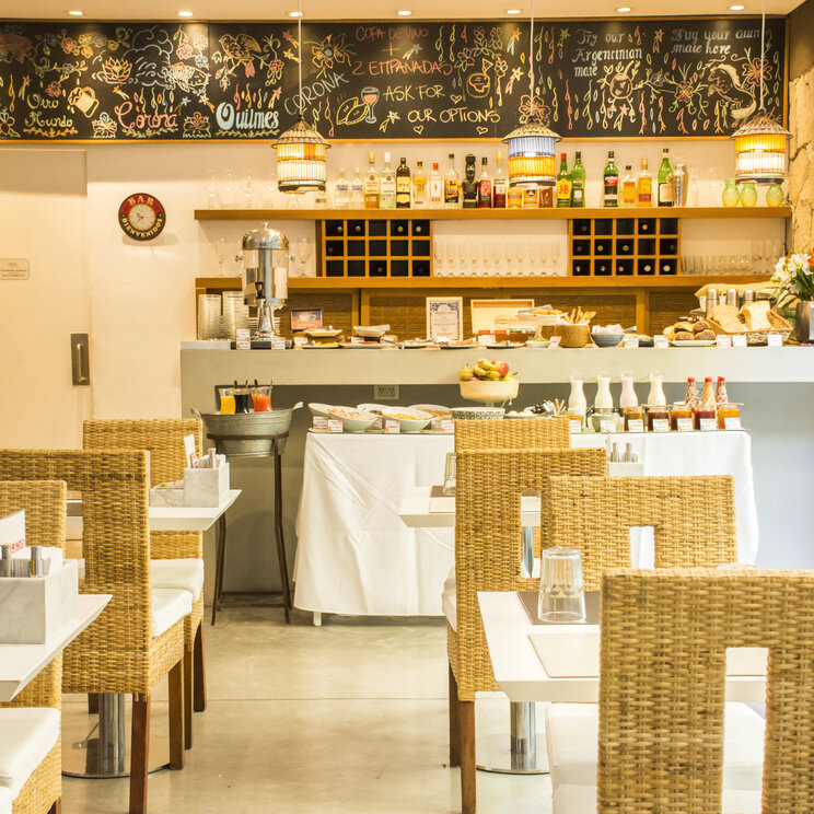 Fruehstuecksbuffet und Bar mit beschriebener Kreidetafel hinter geflochtenen Stuehlen im Mine Hotel in Buenos Aires.
