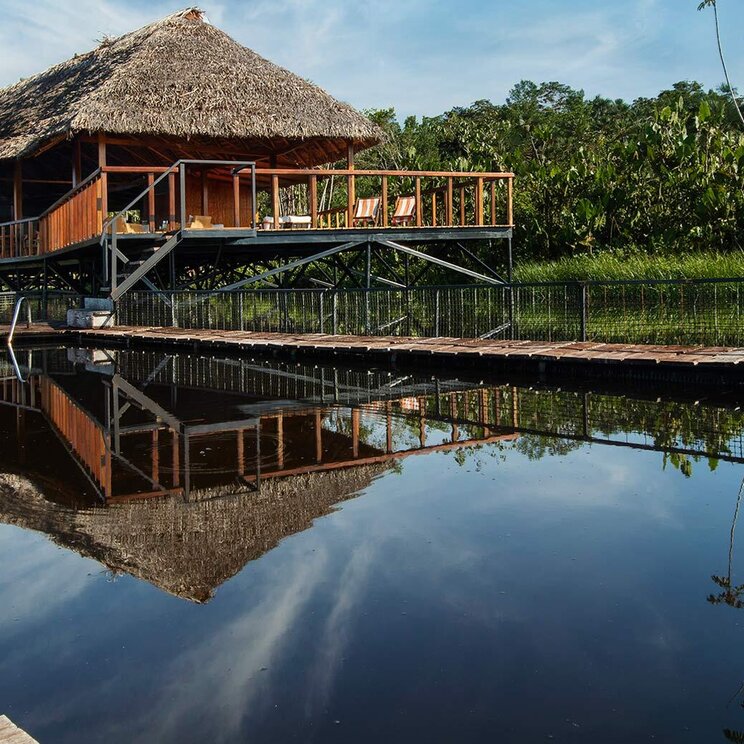 Holzsteg und Pool im See mit Spiegelung des strohgedeckten Hauptgebaeudes, Sacha Lodge, Ecuador.