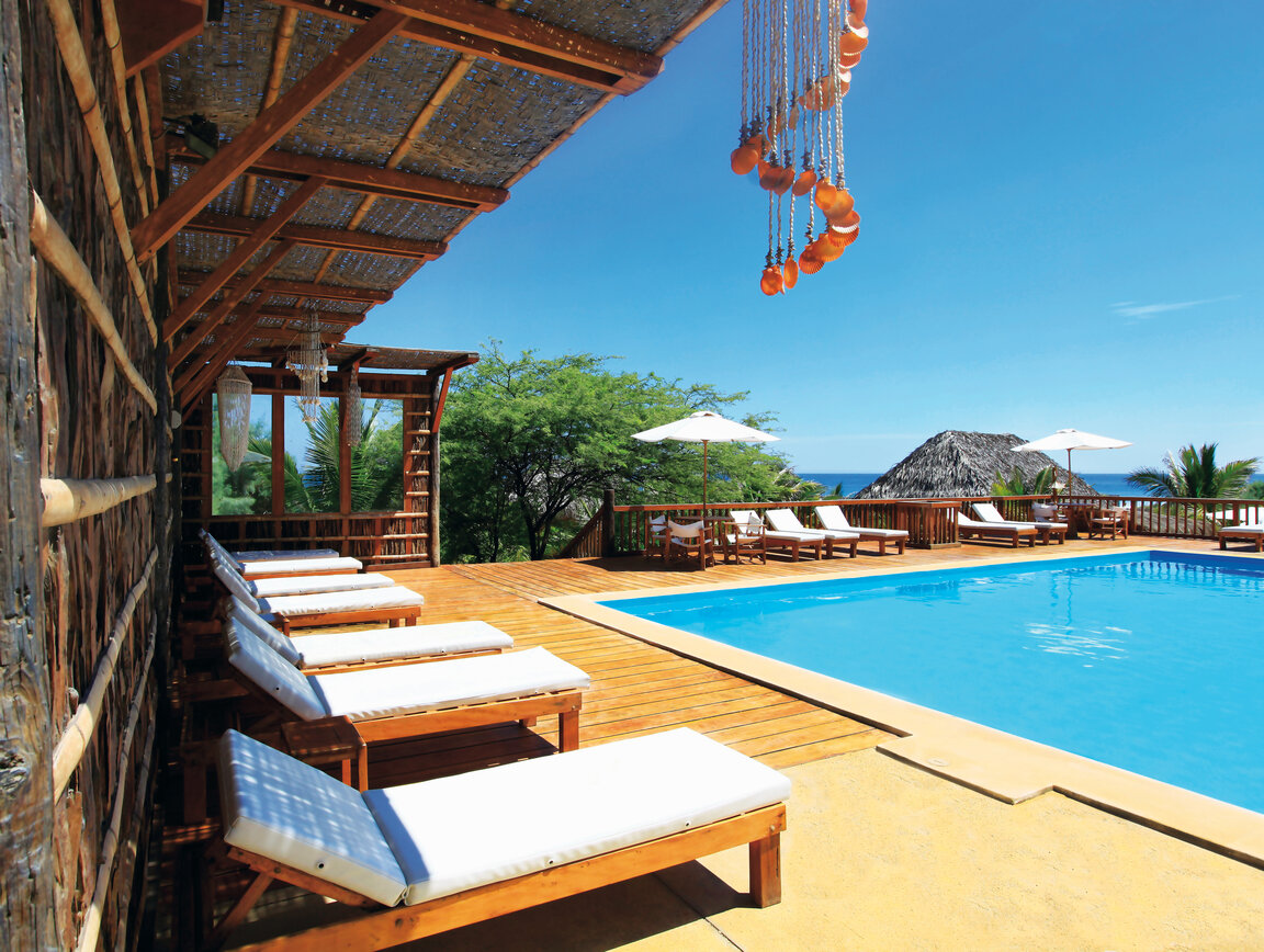 Aranwa: Einreihige Sonnenliegen am blauen Pool, hölzernes Deck und Blick auf den Pazifik.