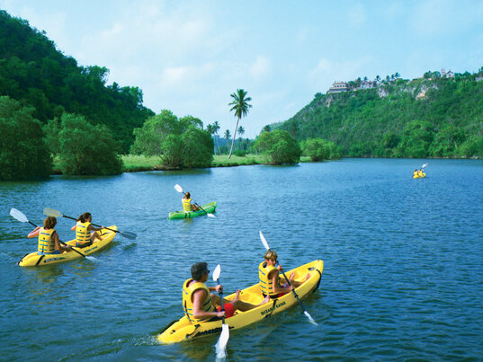 Menschen in gelben Kayaks auf einem tropischen Fluss zwischen gruenen Huegeln, Casa de Campo.