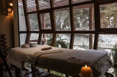 Massageliege vor einer Fensterfront mit Blick auf Felsen und Vegetation im K'intu Spa in Peru.
