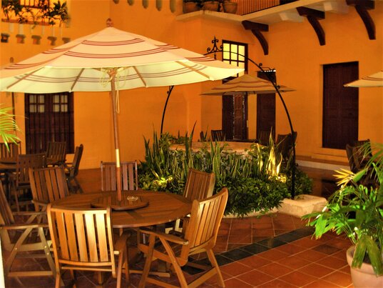 Patio des Hotel Castelmar in Campeche, Mexiko mit Holztischen, Sonnenschirmen und zentralem Brunnen.