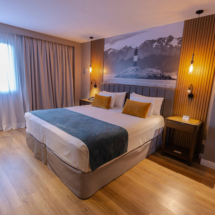 Modernes Zimmer im Hotel Alto Andino in Ushuaia, Argentinien, mit Kingsize-Bett, stilvoller Beleuchtung und Wandbild vom Leuchtturm „Les Eclaireurs“.