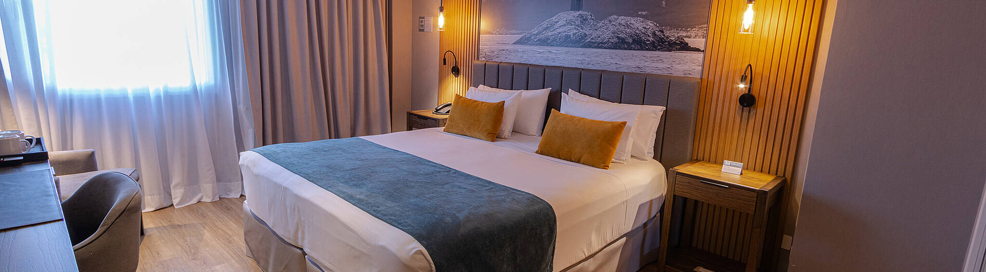 Modernes Zimmer im Hotel Alto Andino in Ushuaia, Argentinien, mit Kingsize-Bett, stilvoller Beleuchtung und Wandbild vom Leuchtturm „Les Eclaireurs“.