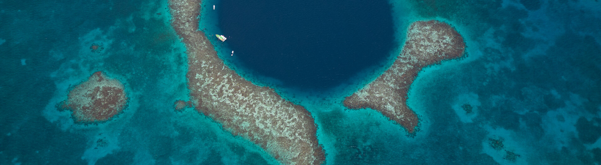 Luftaufnahme des kreisrunden, dunkelblauen Great Blue Hole inmitten von Korallenriffen in Belize.