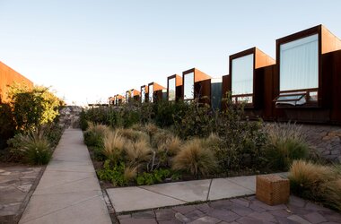 Moderne Hotelgebäude aus Roststahl mit großen Fenstern hinter einem Garten mit Gräsern im Tierra Atacama Chile.