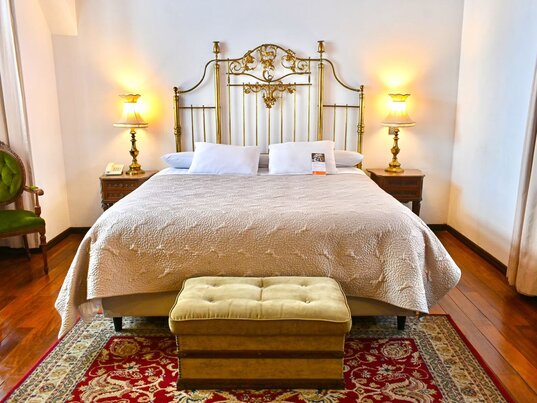 Antikes Messingbett zwischen zwei Nachttischen mit klassischen Lampen im Parador Santa Maria.