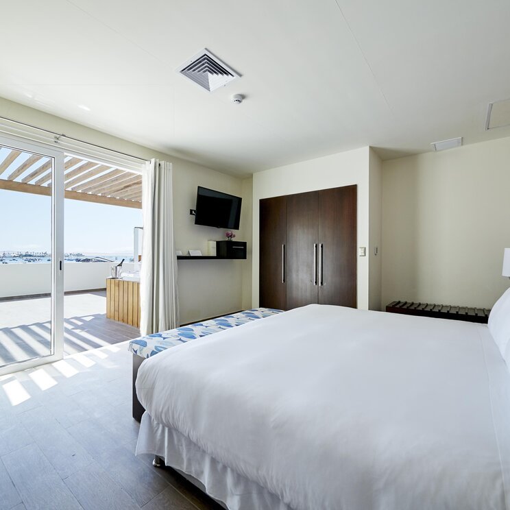 Doppelzimmer mit weißem Bett, Schrank, Fernseher und Balkon mit Meerblick im Aranwa Paracas Resort, Peru.