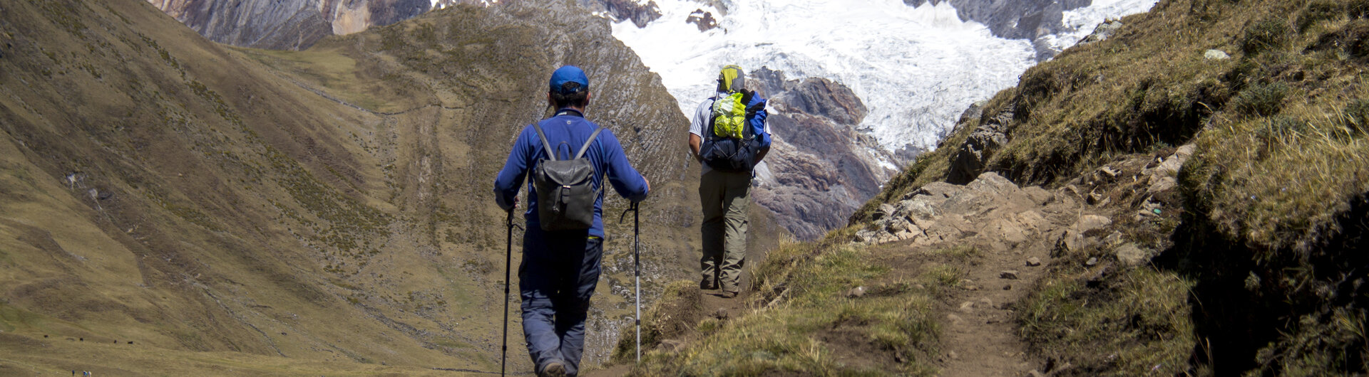 Zwei Wanderer mit Rucksäcken auf einem Pfad bei Huaraz in Peru vor den schneebedeckten Gipfeln der Cordillera Blanca.