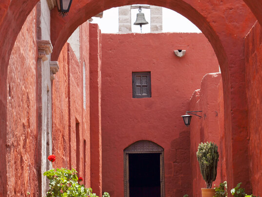 Rote Kolonialarchitektur mit Torboegen, Pflanztoepfen und einer Glocke im Santa-Catalina-Kloster in Arequipa.