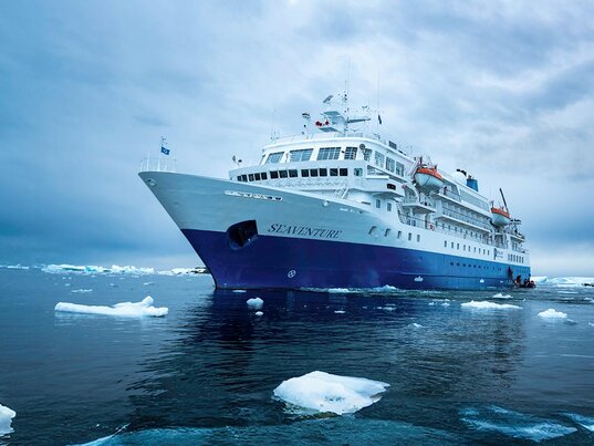Expeditionsschiff Ocean Seaventure in der Antarktis zwischen treibenden Eisschollen auf ruhigem Meer unter bewölktem Himmel.