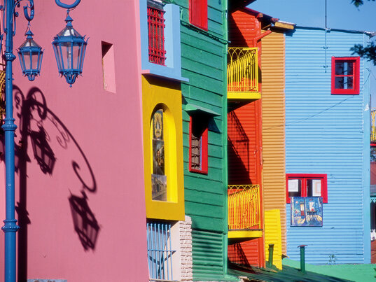 Bunte Wellblechfassaden in Pink, Grün und Blau mit einer Straßenlaterne im Viertel Caminito, Buenos Aires, Argentinien.