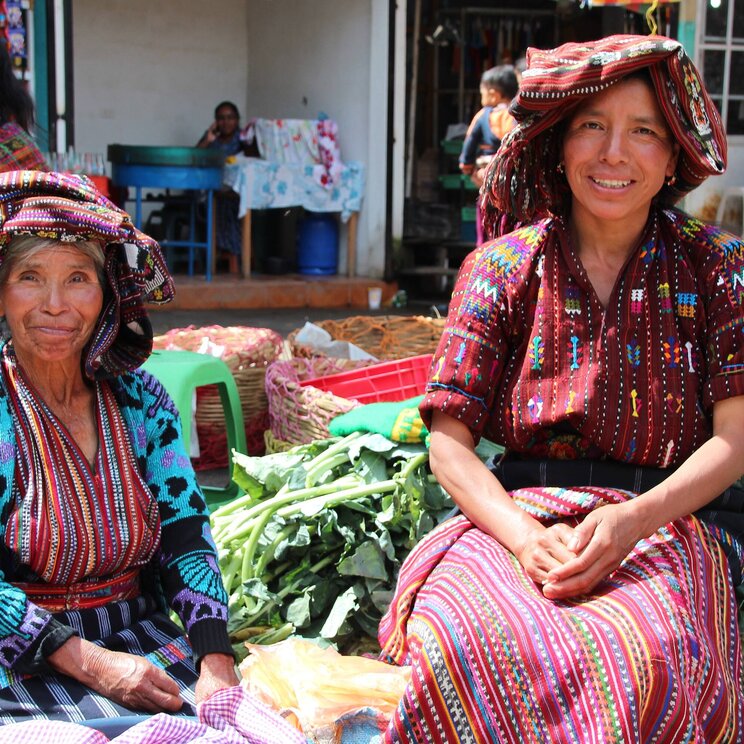 Zwei Frauen in traditionellen Huipiles sitzen auf einem Markt in Guatemala.