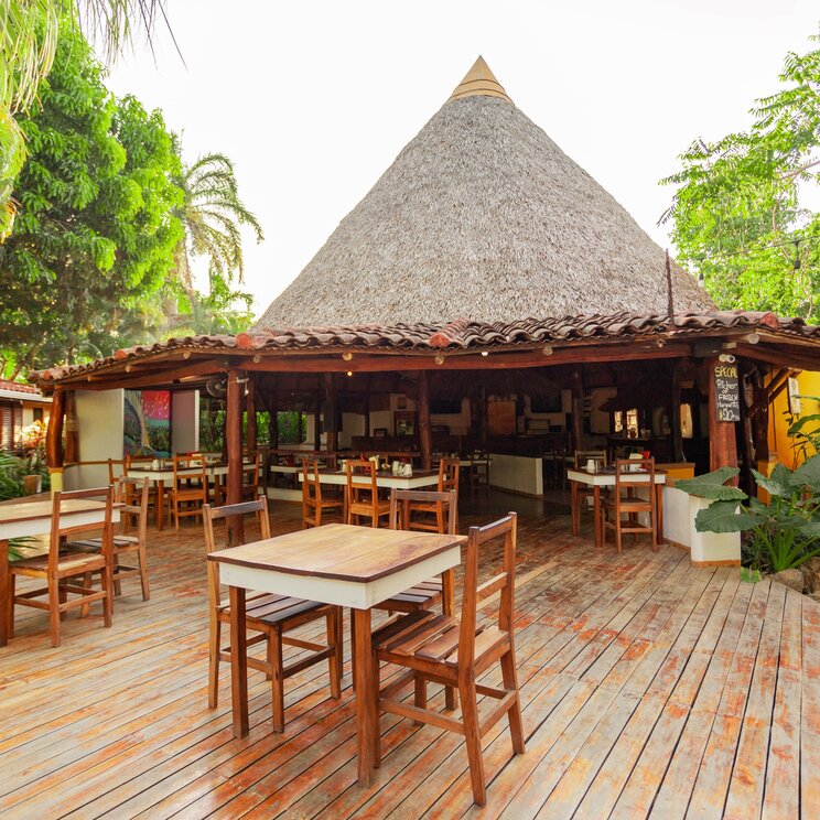Halboffenes Restaurant mit Barhocker-Bereich und Blick in den tropischen Garten des Hotels.