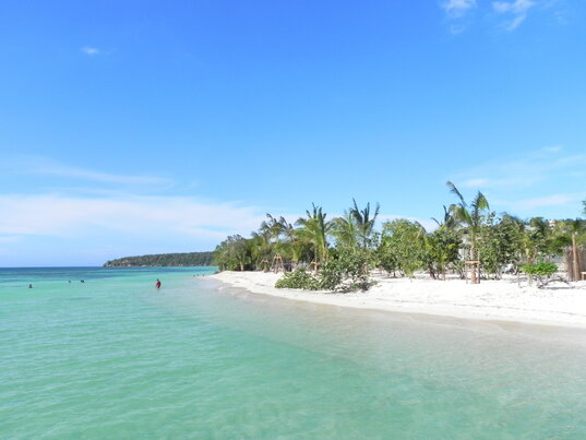 Weißer Sandstrand mit Palmen und Blick auf das hellblaue Meer bei der Punta Rucia Lodge in der Dominikanischen Republik.