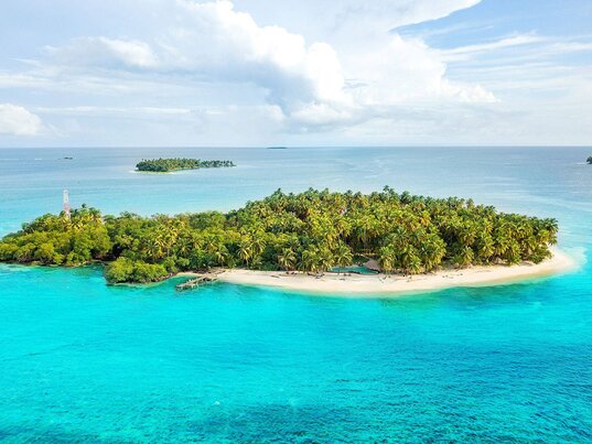 Luftaufnahme der Insel Calala im klaren blauen Wasser mit üppiger Vegetation und einem Sandstrand.
