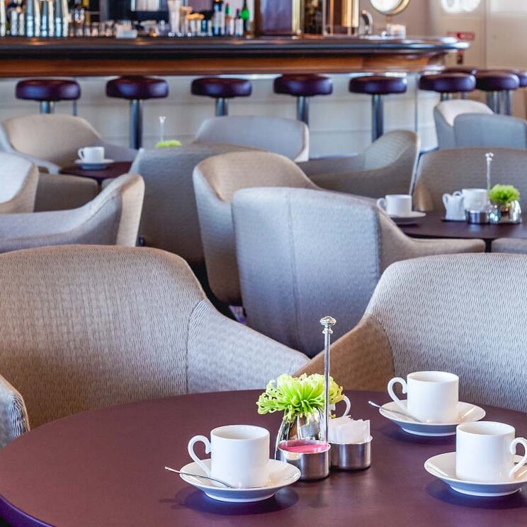 Lounge an Bord der Ocean Seaventure Antarktis Expeditionskreuzfahrt mit bequemen Sesseln, kleinen Tischen und Barbereich im Hintergrund.