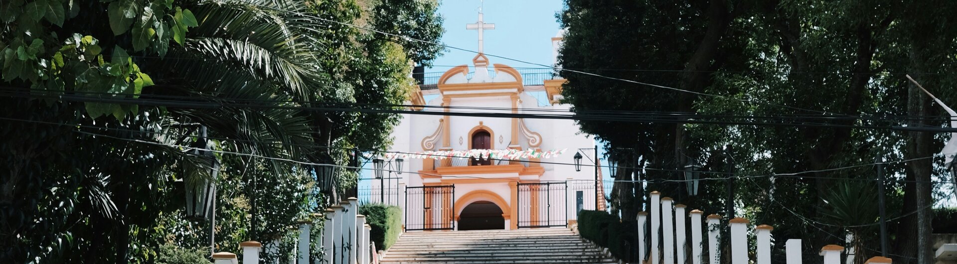 Breite, von Bäumen gesäumte Steintreppe, die hinauf zur Kirche Iglesia de Guadalupe in San Cristóbal, Mexiko führt.